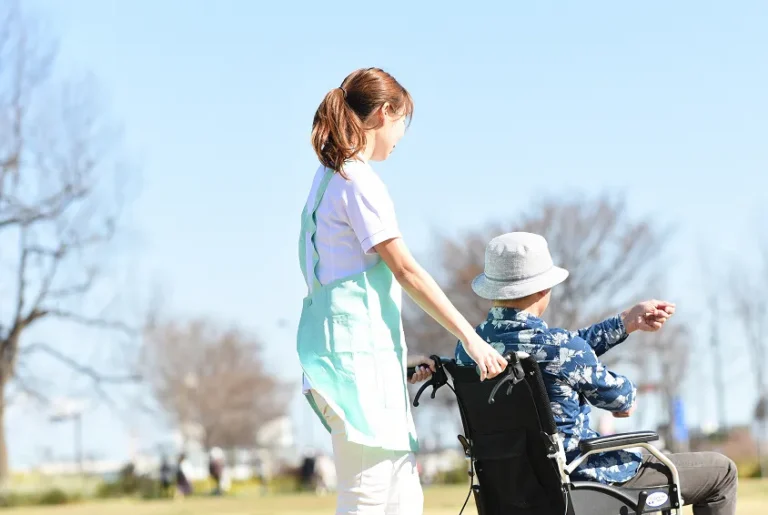 青空のもと老人の車椅子を押す女性